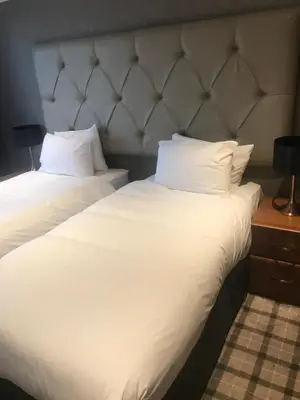two beds in a hotel room with white sheets and pillows at The Scot in Oban