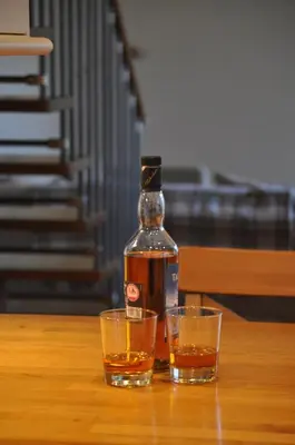 a bottle of whiskey and two glasses on a table at The Old Coach House, Alltshellach Cottages in North Ballachulish