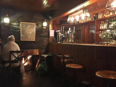 a person sitting at a bar with a fireplace at The Old Coach House, Alltshellach Cottages in North Ballachulish