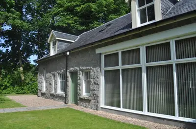 a stone house with large sliding doors on it at The Old Coach House, Alltshellach Cottages in North Ballachulish