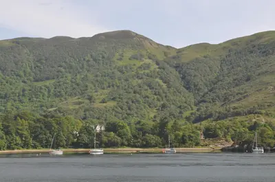 a bunch of boats on the water in front of mountains at The Old Stables, Alltshellach Cottages in North Ballachulish