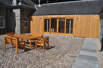 a patio with a wooden table and benches in front of a building at The Old Stables, Alltshellach Cottages in North Ballachulish