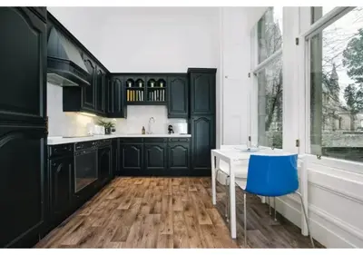 a kitchen with black cabinets and a blue stool at JOIVY Elegant New Town Flat near Princes Street in Edinburgh