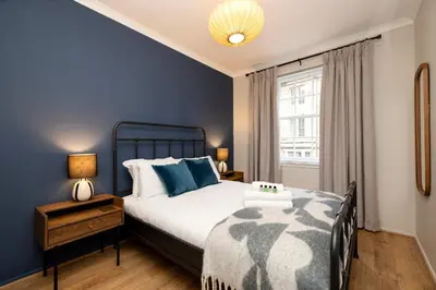 a bedroom with a bed with blue walls and a window at JOIVY Stylish Castle View Flat with Balcony in Edinburgh
