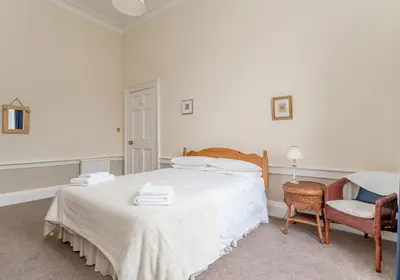 a white bedroom with a bed and a chair at Melville Street Apartment in Edinburgh