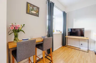 a dining room table with a vase of flowers and a television at Linlithgow Apartment in Linlithgow