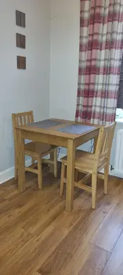 a wooden table and two chairs and a table and a curtain at Millhill St Dunfermline in Dunfermline