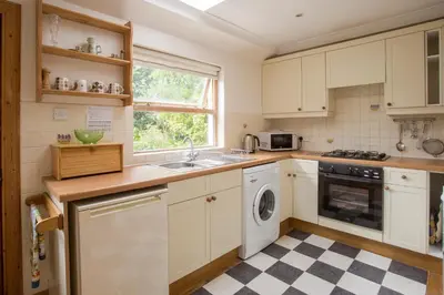 a kitchen with white cabinets and a sink and a dishwasher at Woodcroft Cottage in Ayr