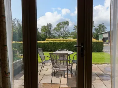 an open door to a patio with a table and chairs at Muirmailing Cottage in Plean