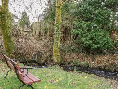 a park bench sitting in the grass next to a tree at The Knowe Lower in Taynuilt