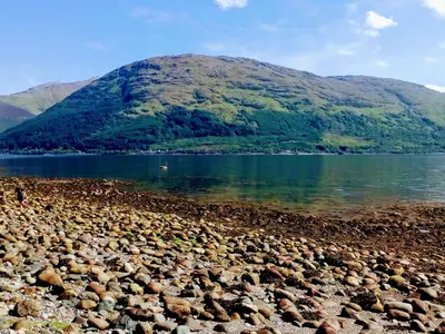 a rocky shore of a lake with a mountain in the background at Pebble Nook in Onich