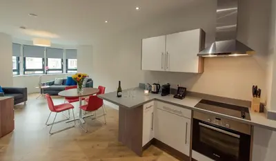 a kitchen with white cabinets and a table with red chairs at PREMIER SUITES PLUS Glasgow Bath Street in Glasgow