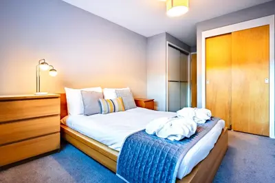 a bedroom with a bed with white sheets and a dresser at Glasgow City Flats in Glasgow