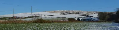 a snow covered mountain with a house and a field at 3 Knocknaha Cottage in Campbeltown