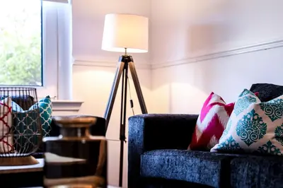 a floor lamp next to a blue couch with pillows at Meadowburn View in Wishaw
