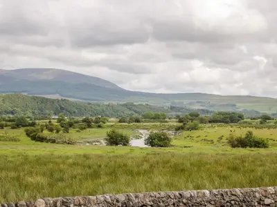 a field with a river and mountains in the background at The Byre in Newton Stewart