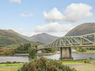 a bridge over a river with mountains in the background at Holly Cottage in Glencoe