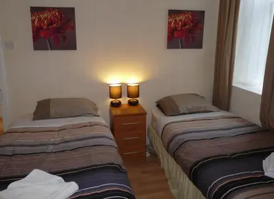 two beds in a room with two lamps on a dresser at Arbour Guest House in Oban