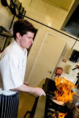 a man in a kitchen preparing food in a stove at Craignelder Hotel in Stranraer