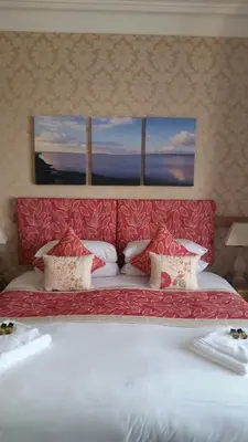 a large bed with a red headboard with two windows at Craignelder Hotel in Stranraer