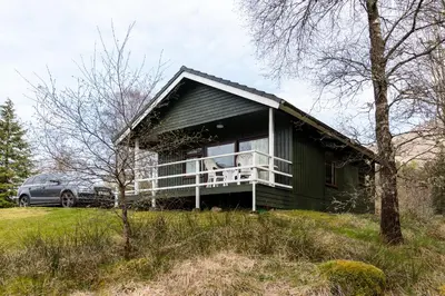 a green house with a car parked in front of it at Heron Lodge sleeps up to 4 with free wifi in Crianlarich
