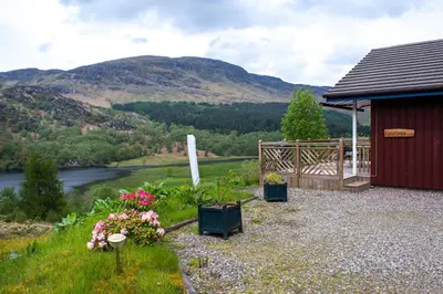 a red shed with flowers and a river and mountains at Kingfisher Lodge with sensational loch views in Crianlarich