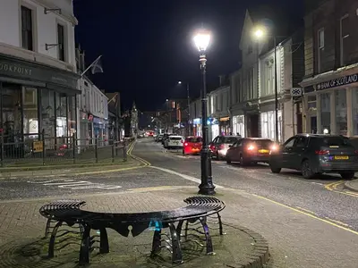 a bench on a city street at night at The Wee Ludging - A Cosy Riverside Cottage for Two in Dunoon