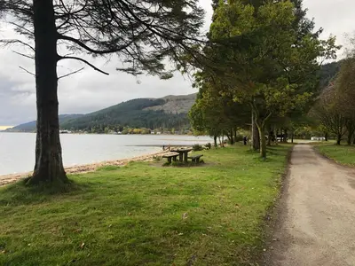 a park with a picnic table next to the water at The Wee Ludging - A Cosy Riverside Cottage for Two in Dunoon