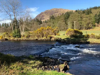 a river with rocks in the water with mountains in the background at The Wee Ludging - A Cosy Riverside Cottage for Two in Dunoon