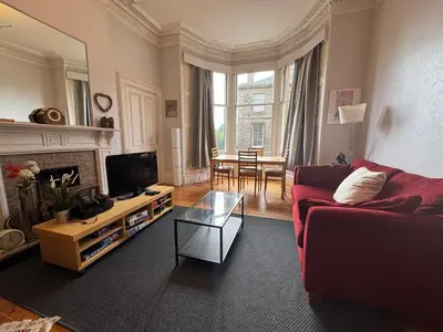 a living room with a red couch and a table at Classic Edinburgh Flat in the heart of Morningside in Edinburgh