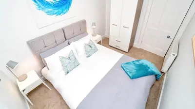 a bedroom with a large white bed with blue pillows at Snug - Tùr Sealladh Apartment in Helensburgh