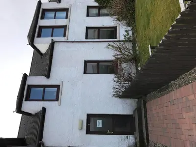 a white building with black windows next to a brick wall at Greannan Upper Self Catering Apartment in Blackwaterfoot