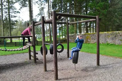 a young boy is sitting on a playground at Callander Woods Holiday Park in Callander