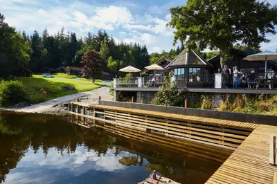 a restaurant with a bridge over a river at LOCH TAY HIGHLAND LODGES and GLAMPING PARK in Morenish