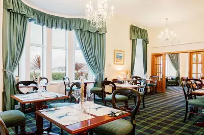 a restaurant with tables and chairs and windows at Muthu Queens Hotel, Oban in Oban