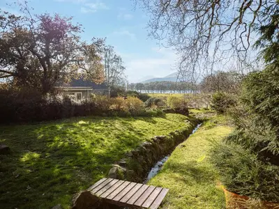 a wooden bench sitting in a field next to a stream at Strathcashel Cottage in Rowardennan