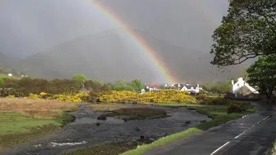 a rainbow over a river with a road and houses at Lochranza Youth Hostel in Lochranza