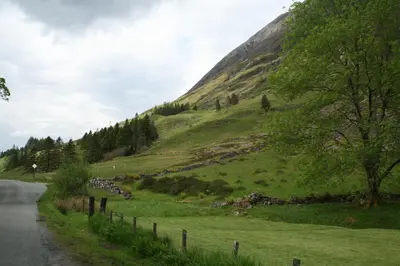 a grassy hill with a fence next to a road at Glencoe Youth Hostel in Ballachulish