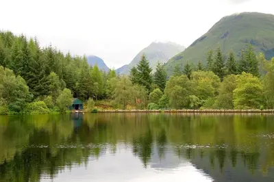 a lake with a cabin in the middle of a forest at Glencoe Youth Hostel in Ballachulish