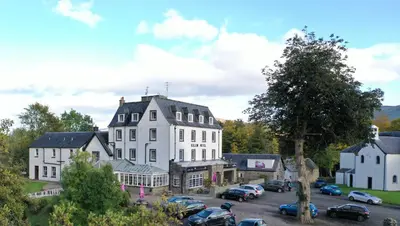 a large white building with cars parked in a parking lot at Killin Hotel in Killin
