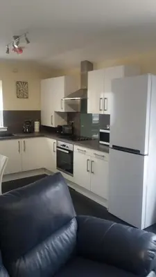 a kitchen with white cabinets and a black leather couch at Ritchie selfcatering in Callander