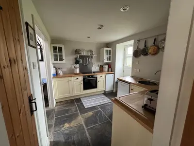 a kitchen with white cabinets and a stove top oven at Charming cottage with loch and hill views nr Edinburgh in Cobbinshaw