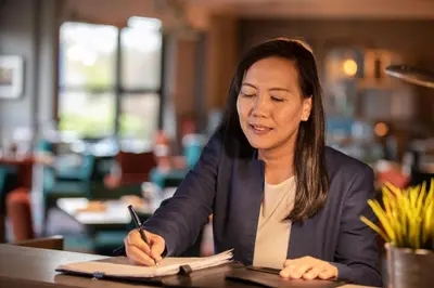 a woman sitting at a table writing in a notebook at DoubleTree by Hilton Edinburgh Airport in Ingliston