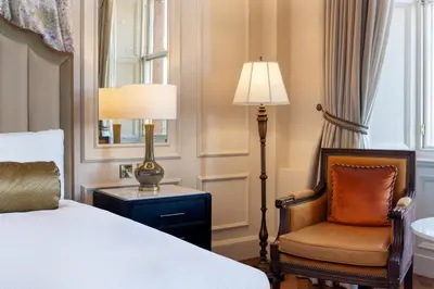 a bedroom with a bed and a chair and a lamp at The Caledonian Edinburgh, Curio Collection by Hilton in Edinburgh