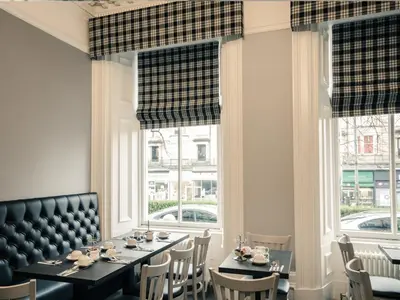 a dining room with tables and chairs and windows at Royal West End Hotel in Glasgow