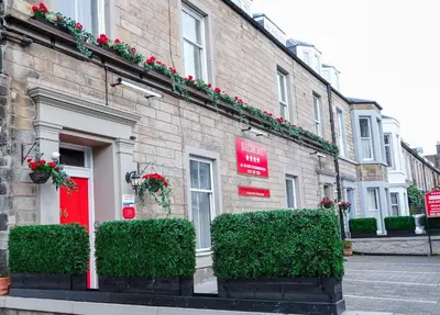 a brick building with red doors and green bushes at Balmore Guest House in Edinburgh