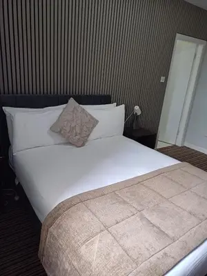 a bedroom with a large bed with white sheets and pillows at Kings Park Hotel in Glasgow
