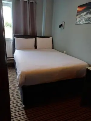 a bedroom with a large bed with white sheets and pillows at Kings Park Hotel in Glasgow