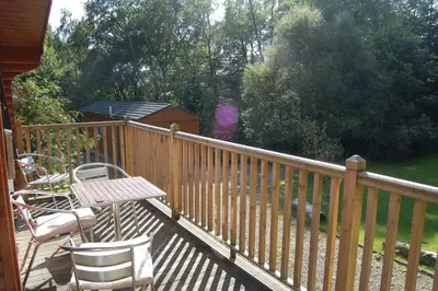 a deck with chairs and a table and a fence at Luxury woodland Alder Lodge in Killin