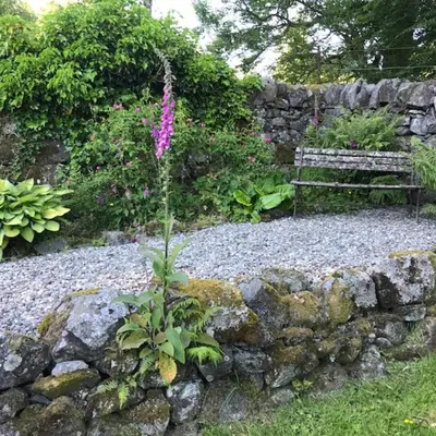 a stone wall with a bench in a garden at Hillside Log cabin, Ardoch Lodge, Strathyre in Strathyre